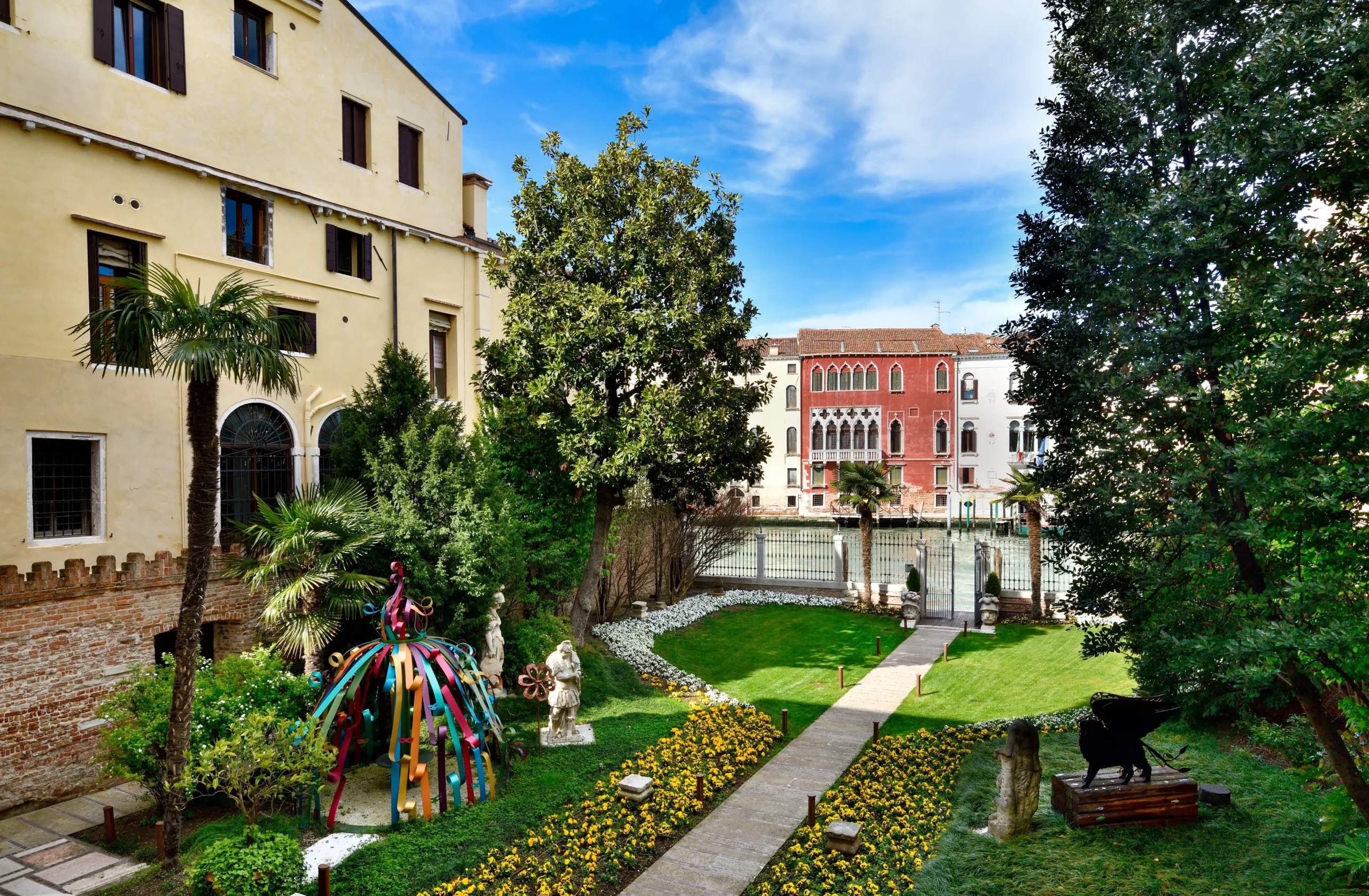 Venart cortile Giardino di Palazzo Venart a Venezia con prato, aiuole fiorite, palme storiche e vista sul Canal Grande