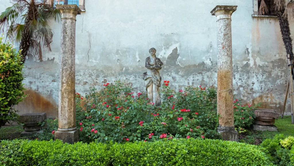 Statua classica tra colonne antiche e roseto fiorito, giardino Palazzo d'Arco Mantova