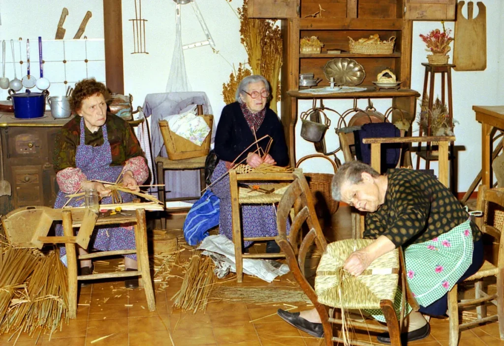 re donne anziane sedute in un laboratorio tradizionale mentre intrecciano manualmente erbe palustri per creare sedie e cesti.